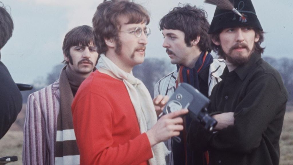 화려한 색상의 옷을 입은 세 남자가 야외에 서 있습니다. 초점이 맞춰진 두 명의 남성, 한 명은 스트라이프 재킷을 입고 다른 한 명은 스카프가 달린 빨간색 셔츠를 입고 있습니다.