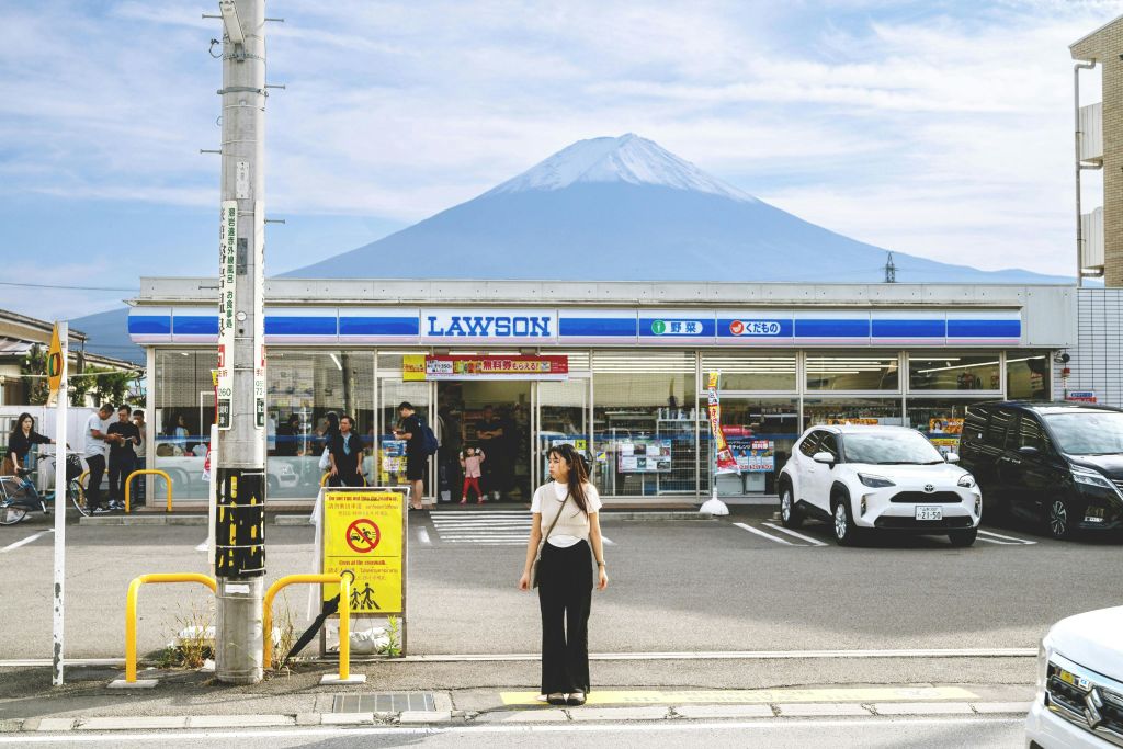 푸른 하늘 아래 배경에 후지산이 보이는 로손 편의점 앞에 한 사람이 서 있습니다.