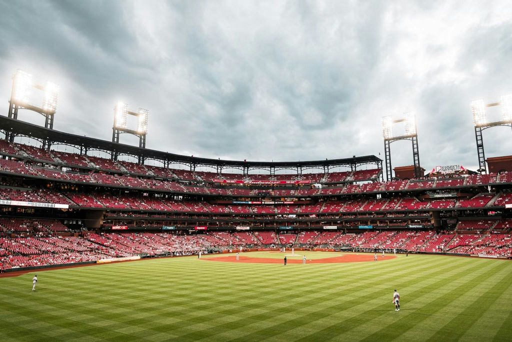 경기가 진행 중인 야구 경기장, 녹색 필드, 관중석이 가득한 빨간색 좌석, 머리 위로 흐린 하늘.