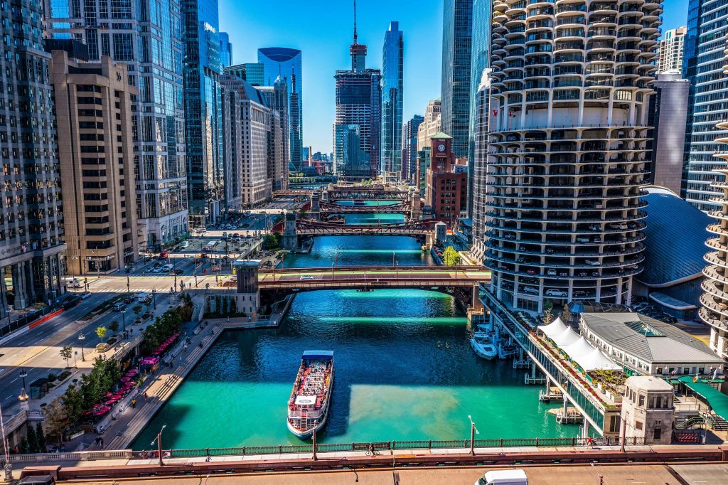 고층 건물, 여러 개의 다리, 강이 있는 도시 풍경. 아래쪽의 맑고 푸른 바다에서 투어 보트를 타고 항해하고 있습니다.