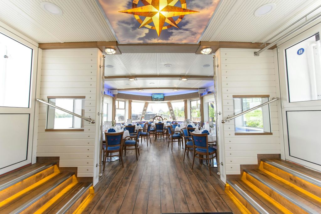 나무 바닥, 파란색 쿠션 의자, 밝은 천장 나침반이 있는 보트의 우아한 식사 공간.