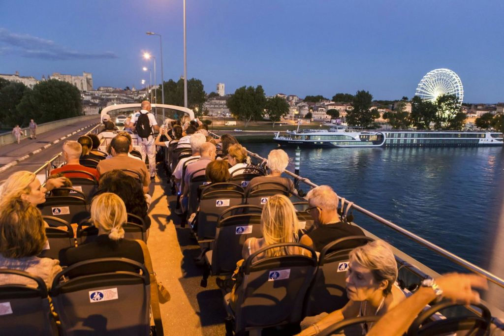 커다란 대관람차와 정박한 유람선을 배경으로 해질 무렵 탁 트인 보트에 앉아 있는 사람들.