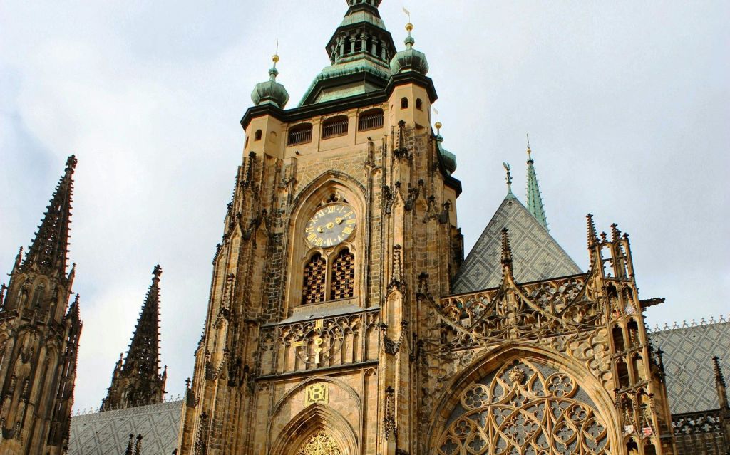 탁한 하늘을 배경으로 시계와 섬세한 건축 조각이 돋보이는 화려한 고딕 양식의 대성당 정면.