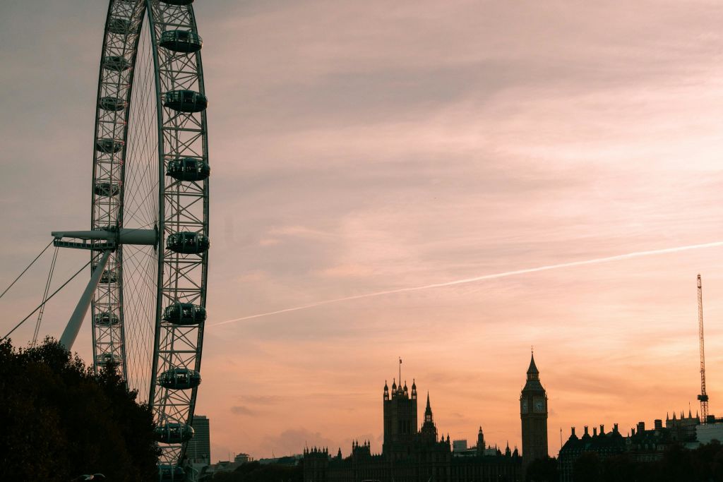 빅벤을 비롯한 대관람차와 고딕 양식의 건물은 분홍색과 주황색의 석양 하늘을 배경으로 실루엣으로 꾸며져 있습니다.