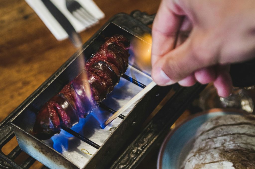 한 사람이 푸른 불꽃이 있는 작은 탁상 그릴에서 나선형으로 자른 구운 고기 꼬치를 요리합니다.