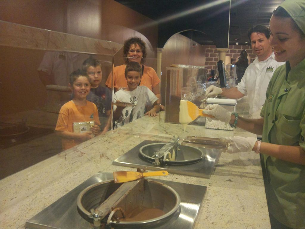 아이스크림 기계와 장갑을 낀 서버를 배경으로 세 명의 미소 짓는 아이들과 카운터 뒤에 서 있는 어른.