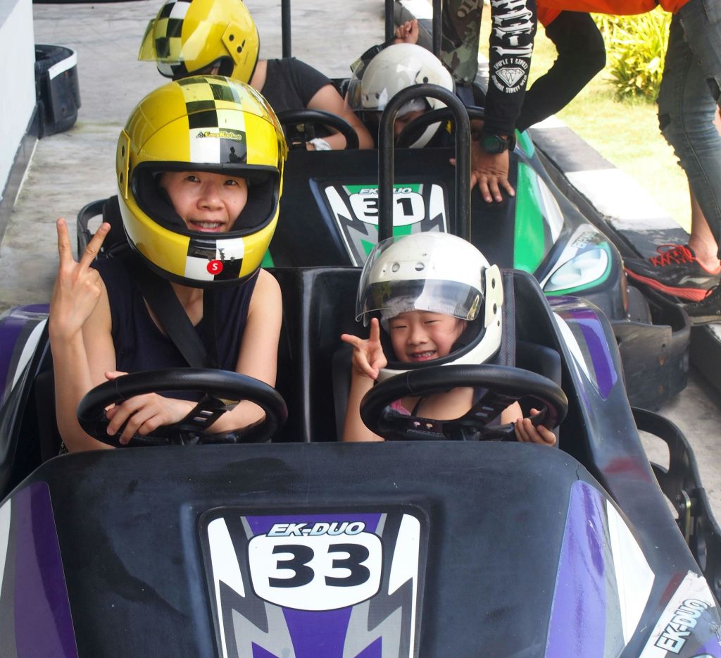 헬멧을 쓴 두 사람이 33번 고카트에 앉아 평화 표지판을 만들고 있습니다. 백그라운드에서 다른 이미지가 표시됩니다.