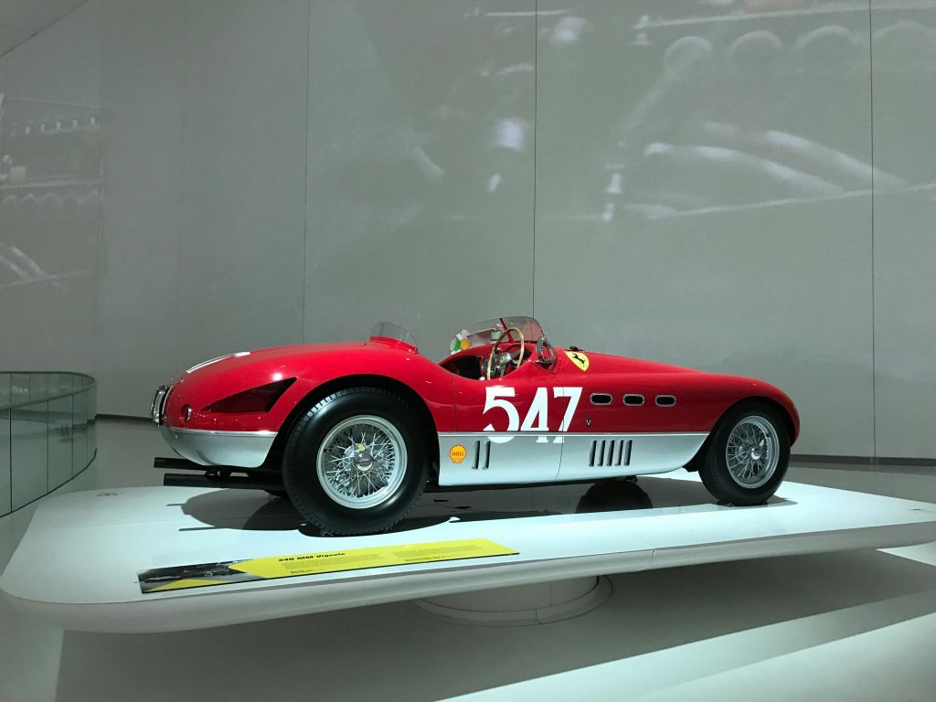 측면에 "547" 이 있는 빈티지 빨간색과 흰색 경주용 자동차로, 박물관과 같은 분위기의 흰색 플랫폼에 전시되어 있습니다.
