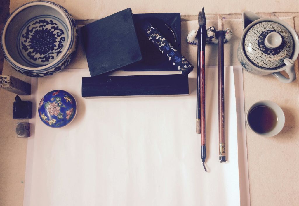 브러시, 잉크 스톤, 도자기 접시를 포함한 미술 용품이 백지 주위에 배치되어 있습니다.