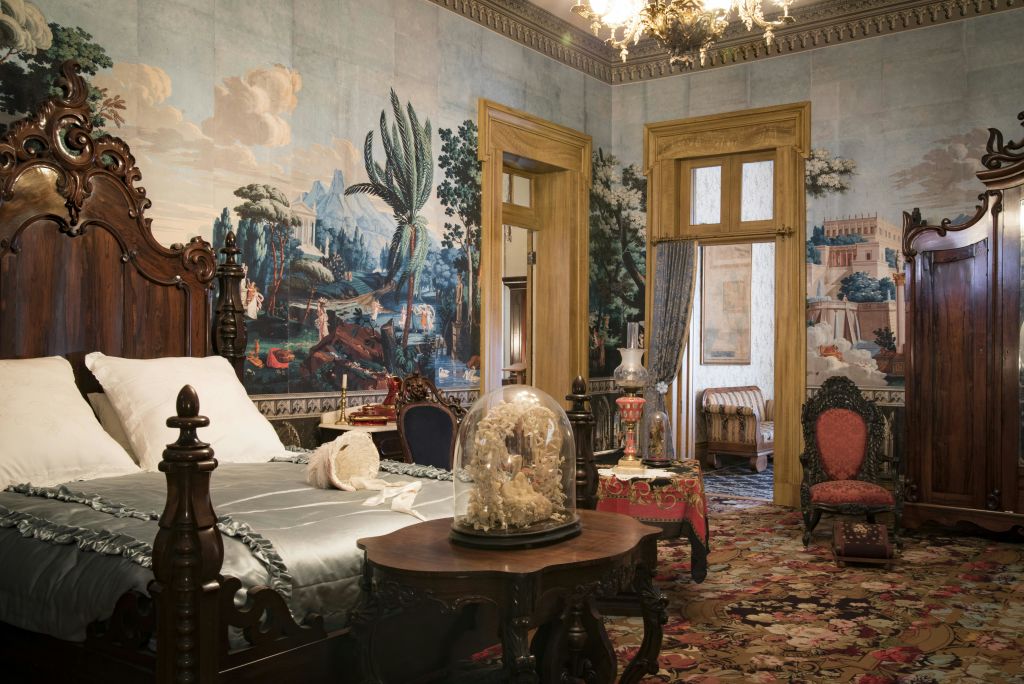 앤티크 가구, 벽화 벽지, 샹들리에, 테이블의 유리 돔 아래 장식품이 있는 화려한 침실.