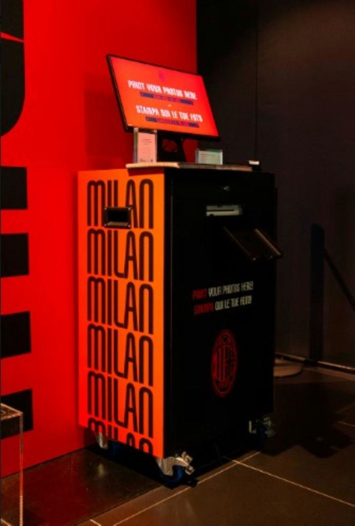 '밀라노' 라는 글자가 굵은 글씨로 반복된 검은색과 빨간색 사진 부스가 실내에 있습니다.