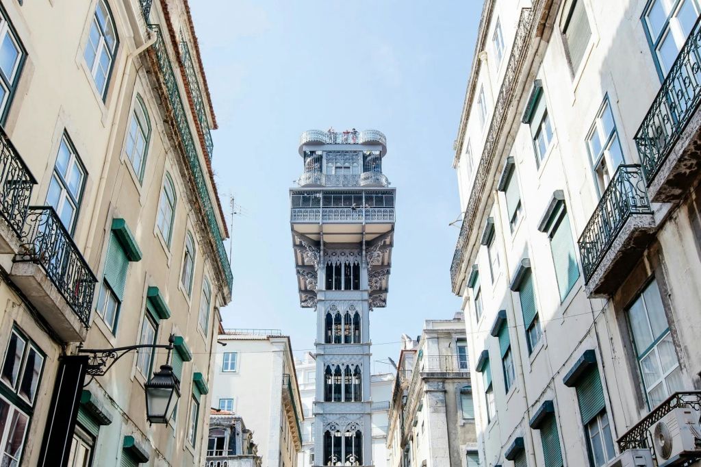 맑고 푸른 하늘 아래 베이지색 건물과 흰색 건물 사이에 역사적인 철제 엘리베이터 타워가 있습니다.