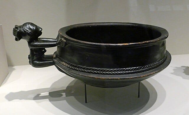 정교한 브레이드 디자인과 디스플레이 스탠드의 손잡이가 있는 블랙 앤티크 그릇입니다.