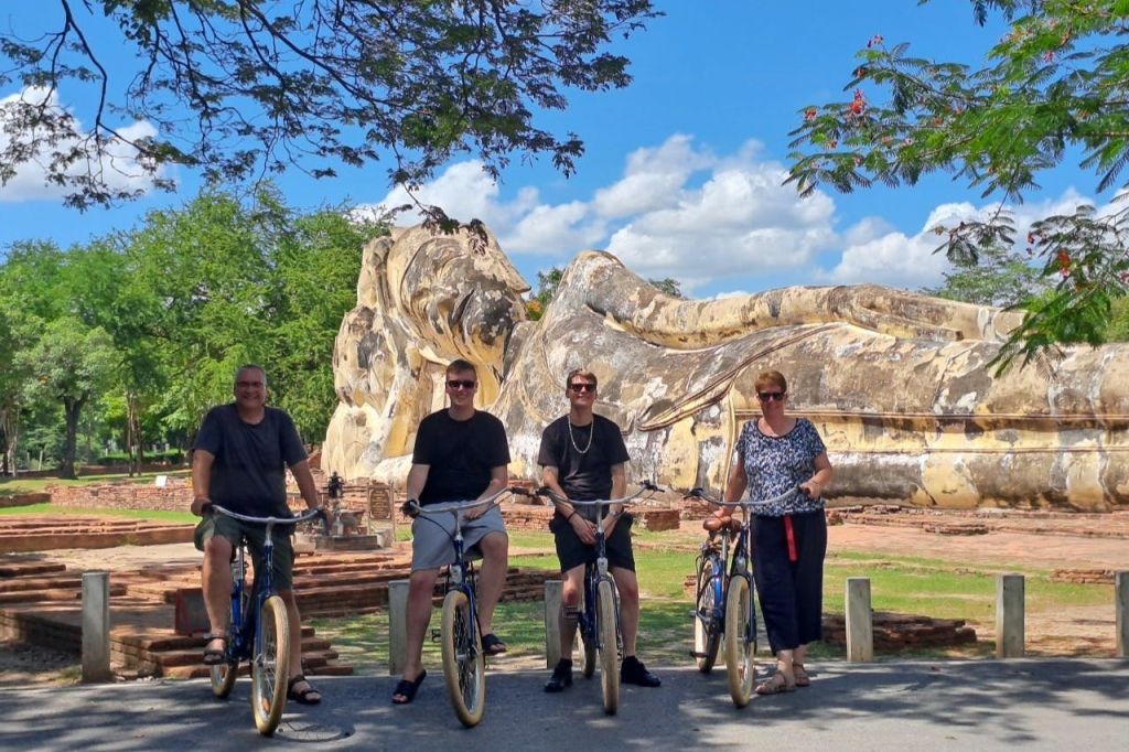 화창한 날 공원의 커다란 안락한 석상 앞에서 포즈를 취하는 자전거를 탄 네 사람.