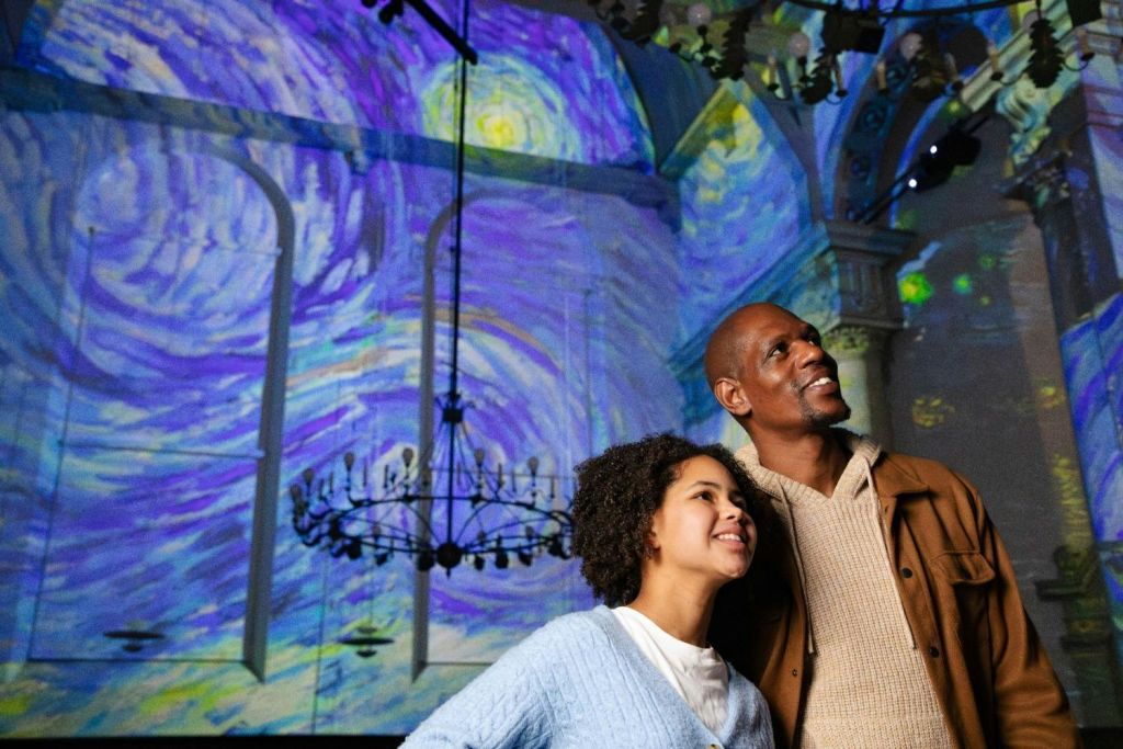 장식용 샹들리에와 기둥이 있는 실내 환경에서 화려한 투영 아래에 서 있는 두 사람.