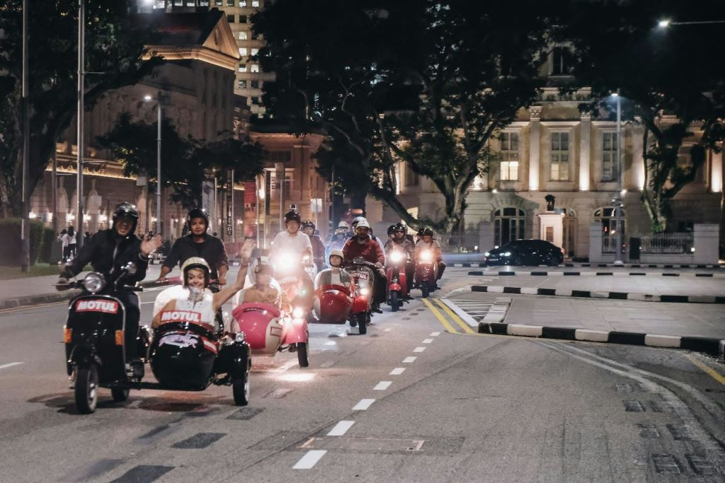 밤에 도시의 거리에서 사이드카를 타고 모터 스쿠터를 타는 사람들, 건물과 나무를 배경으로.