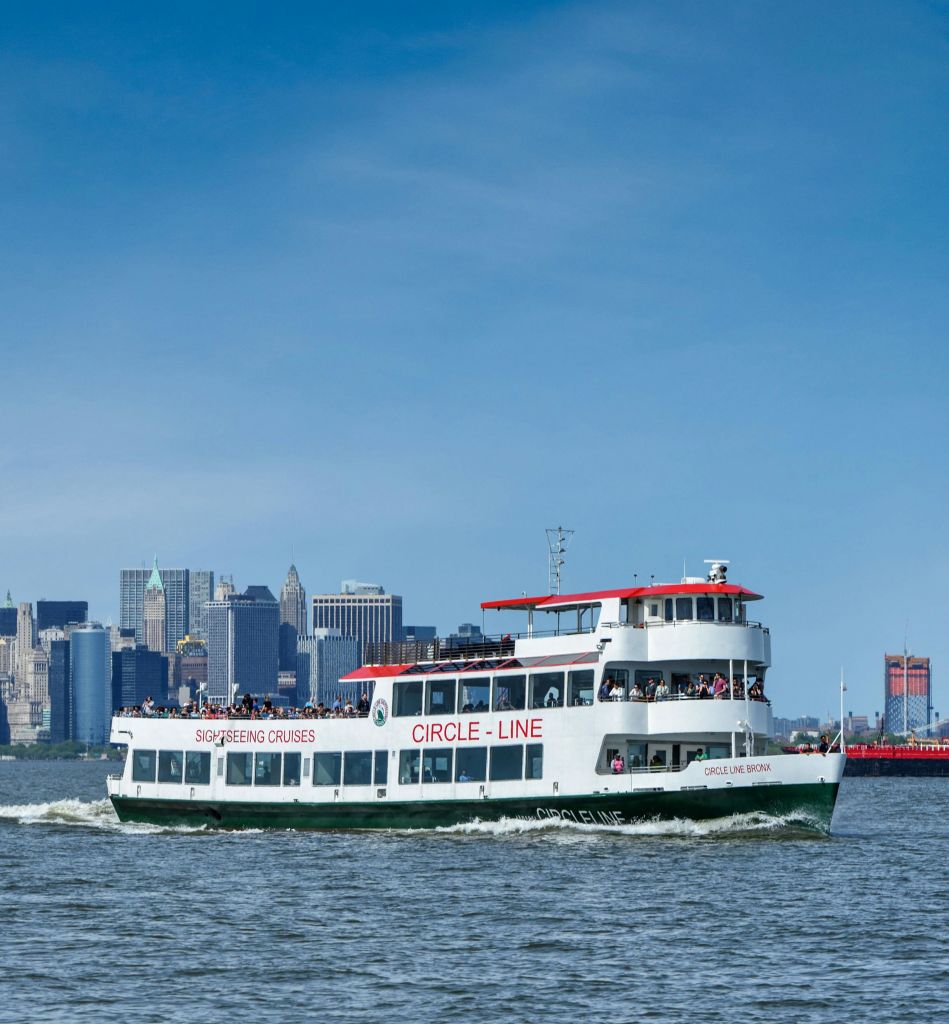 맑고 푸른 하늘 아래 도시 스카이라인을 배경으로 '서클 라인' 이라는 이름의 관광 크루즈 보트가 물 위를 항해합니다.