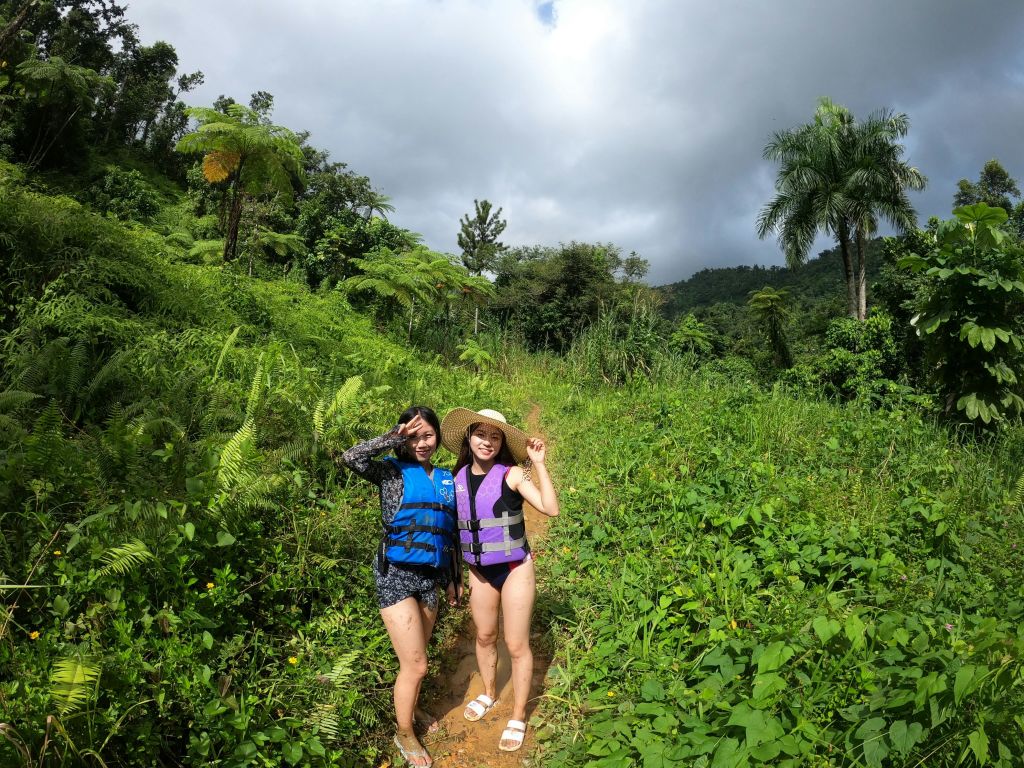 머리 위로 흐린 하늘이 펼쳐진 울창하고 푸른 정글에서 구명조끼를 입은 두 사람이 포즈를 취하고 있습니다.
