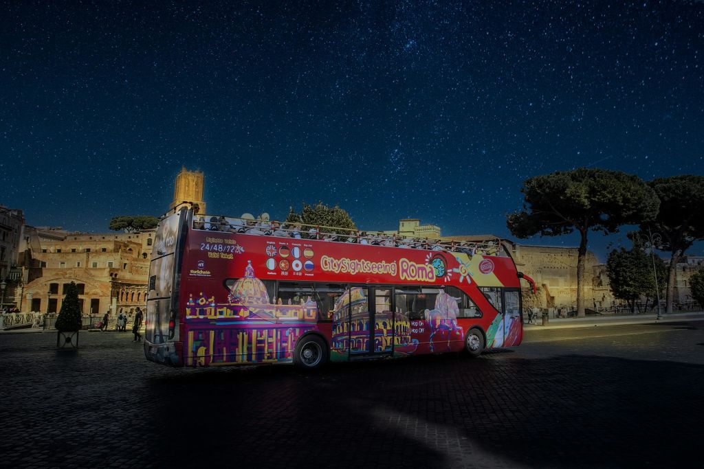 밤에는 별이 빛나는 하늘과 역사적인 건물을 배경으로 로마의 빨간색 2층 관광 버스가 있습니다.