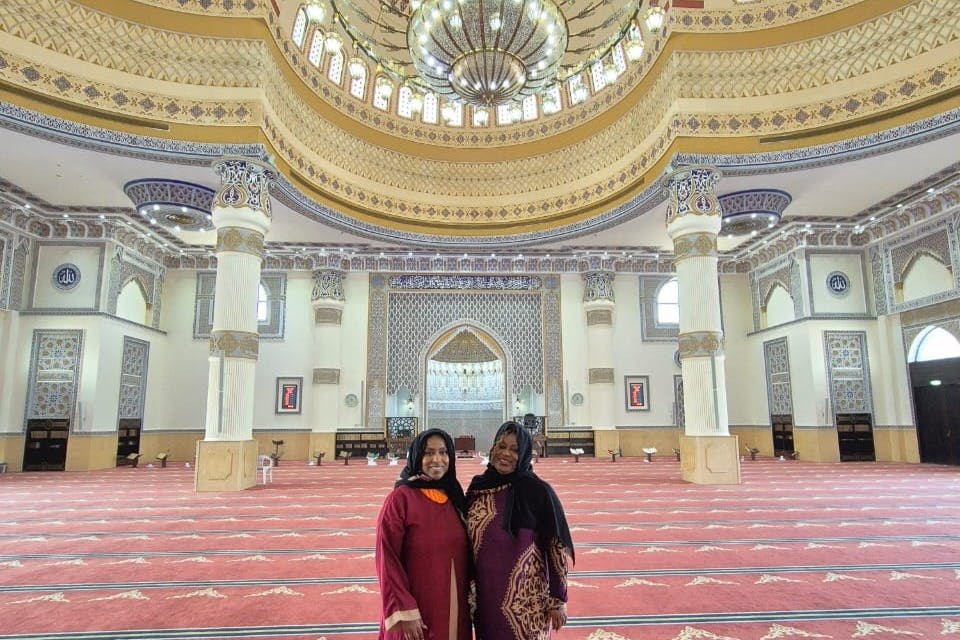 정교한 디자인, 커다란 기둥, 돔형 천장이 있는 웅장한 모스크 내부에는 전통 복장을 한 두 명의 여성이 서 있습니다.