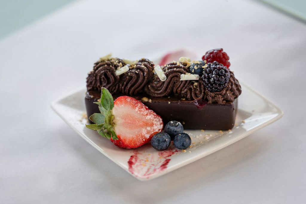 화이트 플레이트 위에 파이 초콜릿 무스, 베리, 화이트 초콜릿 쉐이빙을 얹은 직사각형 초콜릿 디저트입니다.