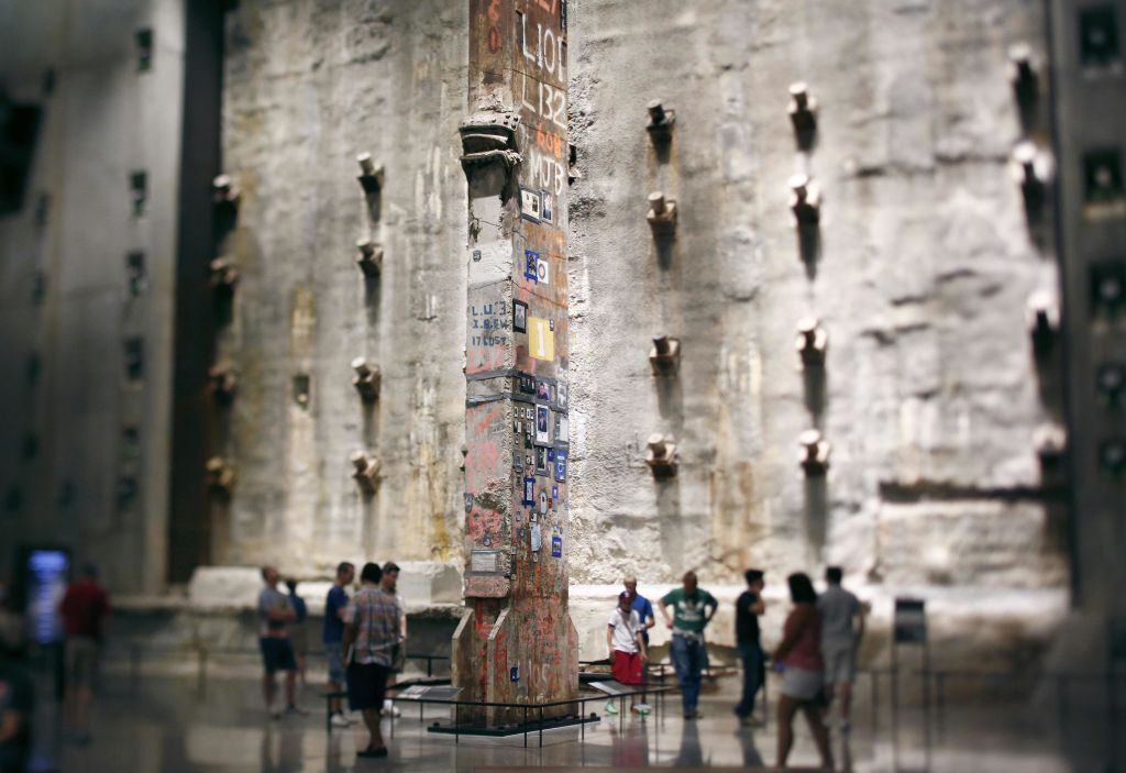 사람들은 험준한 회색 콘크리트 벽이 있는 크고 산업적으로 보이는 방에서 높고 장식된 강철 기둥을 관찰합니다.