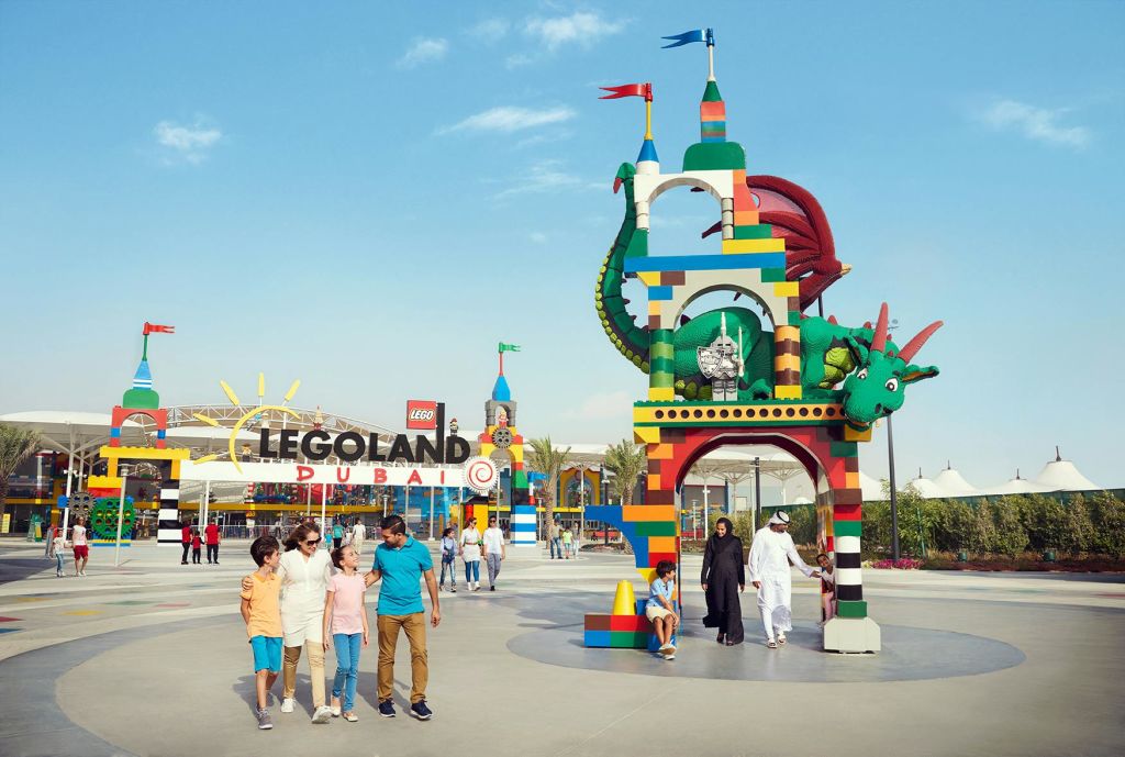 가족들은 화창한 날 레고랜드 두바이 (LEGOLAND Dubai) 에서 용으로 장식된 화려한 입구 아치길 근처를 거닐고 있습니다.
