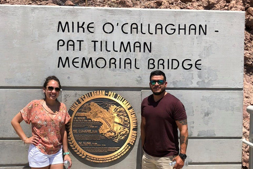 "Mike O'Callaghan-Pat Tillman Memorial Bridge" 문구와 기념패가 있는 벽 앞에 두 사람이 서 있습니다.