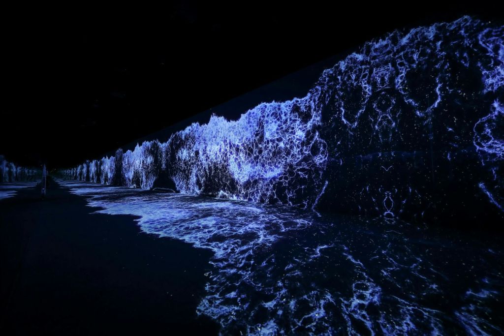 파란색과 흰색 디지털 웨이브가 투사되어 어두운 벽과 바닥을 따라 역동적인 바다 장면을 연출합니다.