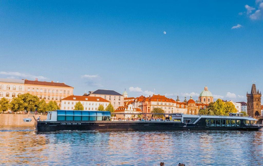 역사적인 건물, 정박된 보트, 맑고 푸른 하늘이 있는 활기찬 강변 풍경.