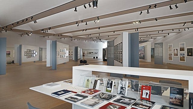 흰색 디스플레이 테이블에 아트 북, 벽에 액자 사진, 천장 스포트라이트가 있는 현대적인 갤러리 인테리어.