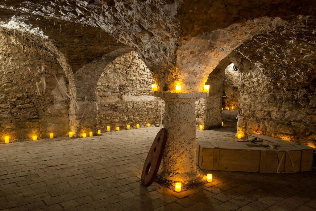 바닥과 선반에 놓인 수많은 작고 빛나는 촛불로 아치형 통로가 있는 오래된 석조 지하실.