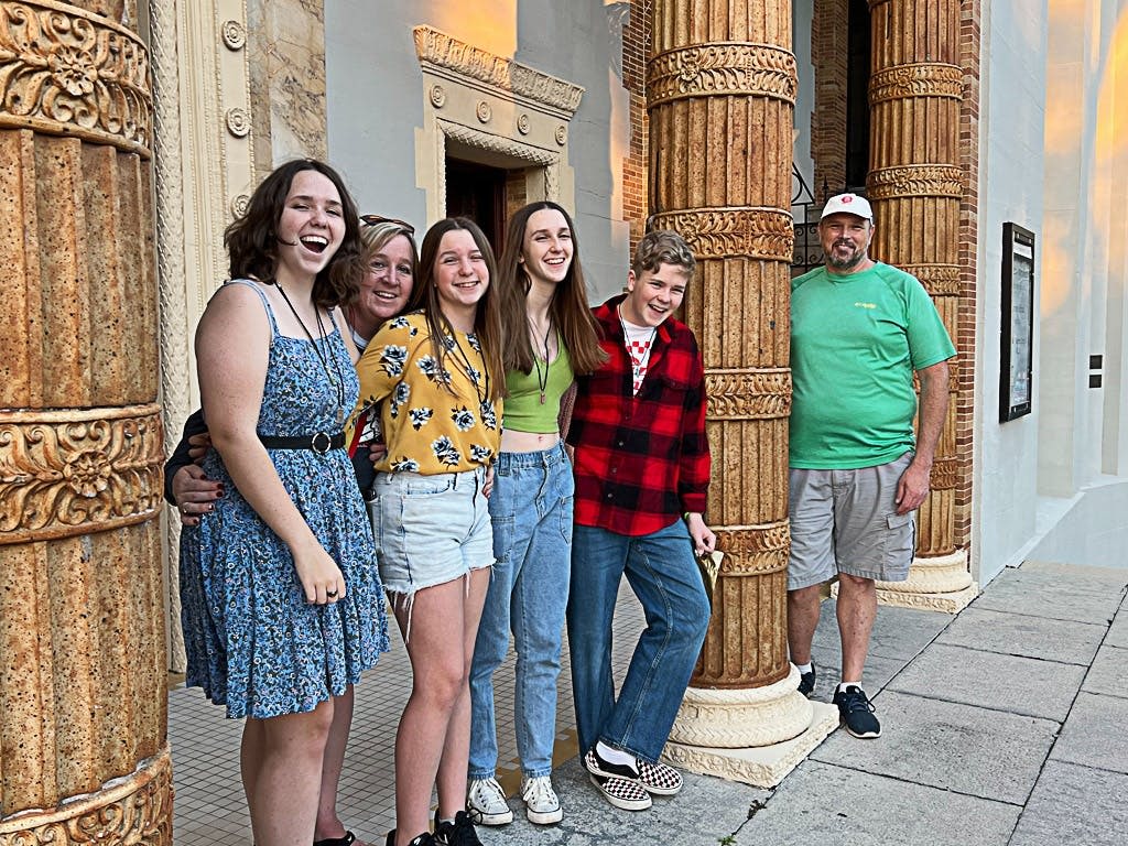 화려한 기둥과 장식 디테일이 있는 건물 앞에 여섯 명이 함께 서서 미소를 짓고 있습니다.