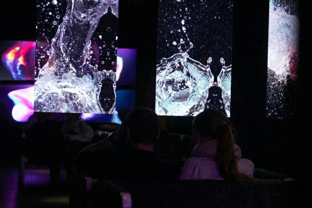 어두운 방에 앉아 있는 두 사람. 커다란 화면에 물 튀김 이미지가 배경으로 표시됩니다.