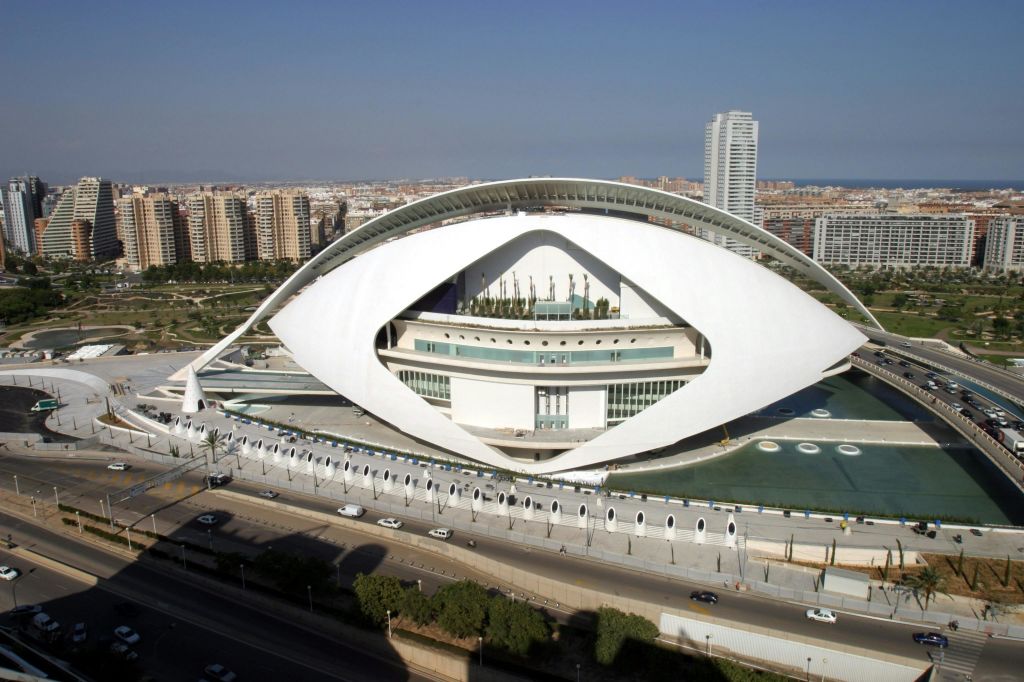 바다로 둘러싸인 눈 모양의 미래 지향적인 흰색 건물로, 도시 풍경과 높은 건물이 배경으로 펼쳐집니다.