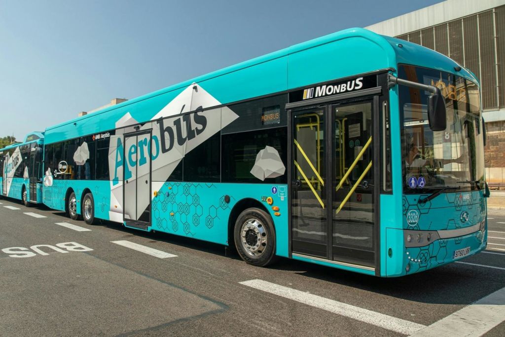 건물 옆 콘크리트 표면에 주차된 측면에 "Monbus" 가 있는 "Aerobus" 라고 표시된 청록색 버스입니다.