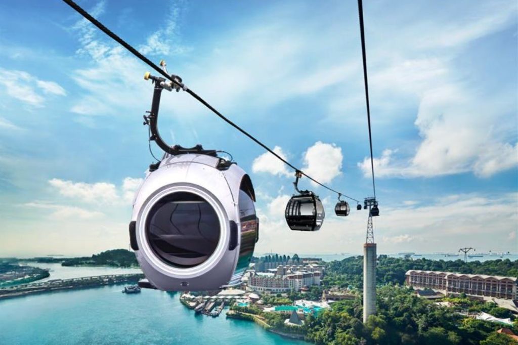 부분적으로 흐린 하늘 아래 도시 풍경과 녹지를 배경으로 물 위를 여행하는 현대적인 디자인의 케이블카.