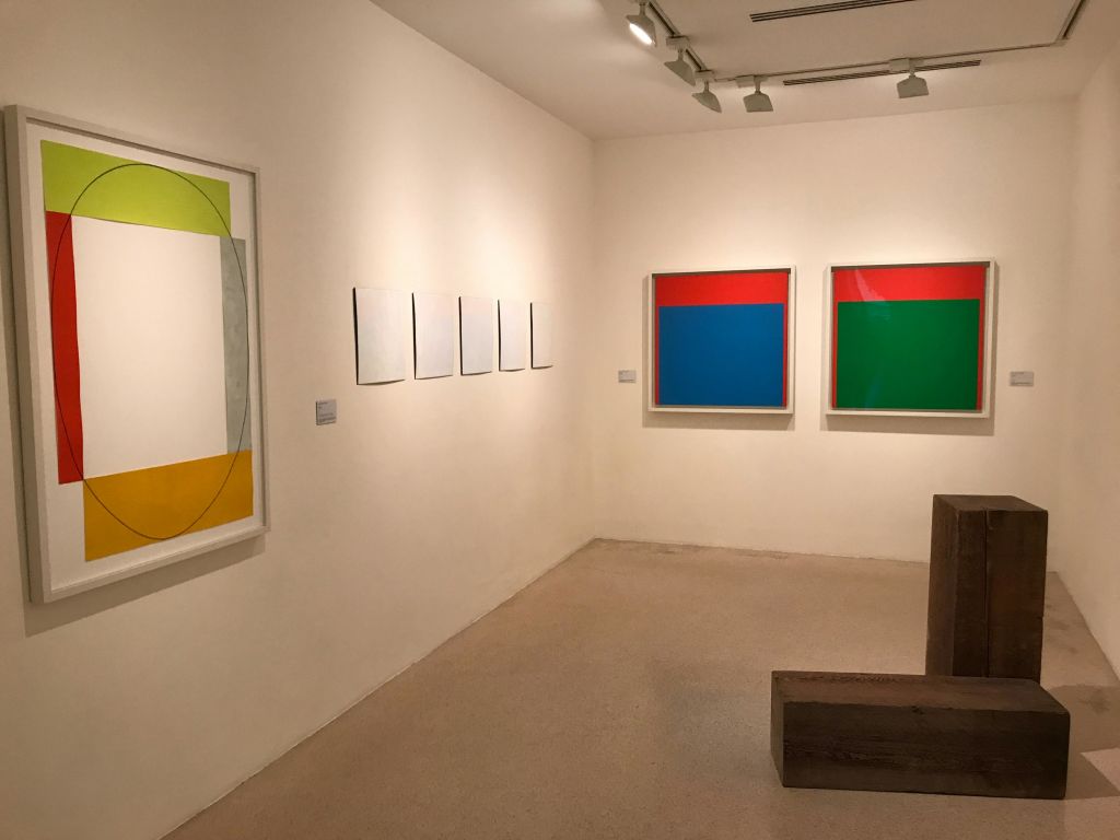 벽면에는 추상화, 전경에는 나무 벤치가 있는 갤러리 룸입니다.