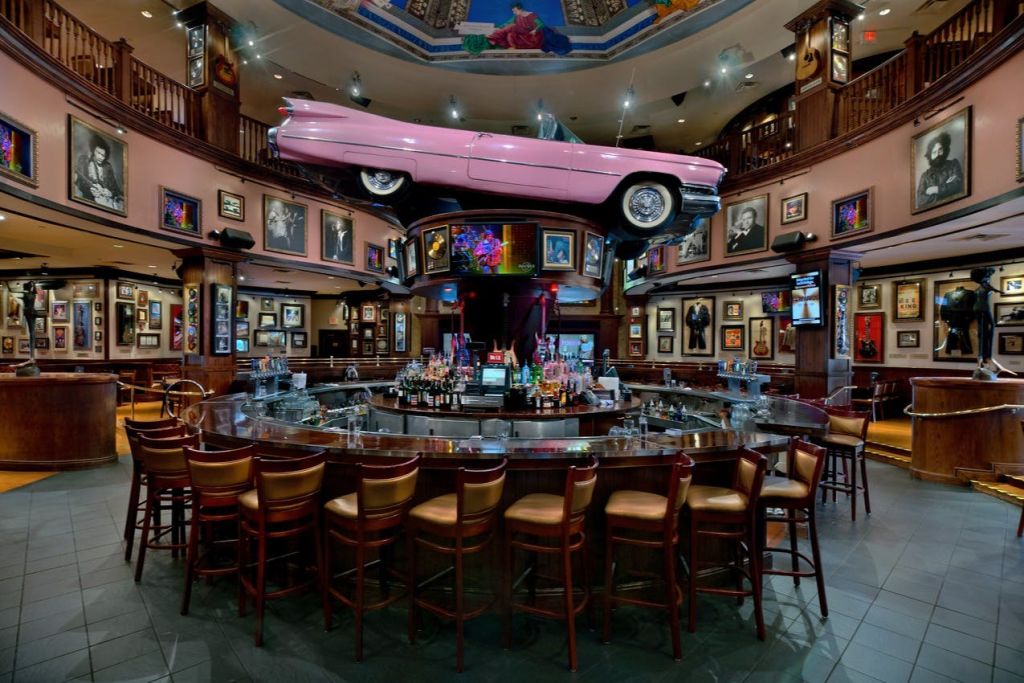 사진과 그림으로 둘러싸인 머리 위로 분홍색 자동차가 놓인 바가 있으며, 카운터에는 빈 의자가 있습니다.