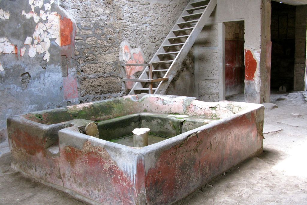 계단을 올라가고 오래된 석고 벽이 있는 소박한 방에 빨간색과 녹색 톤의 석조 분지가 있습니다.