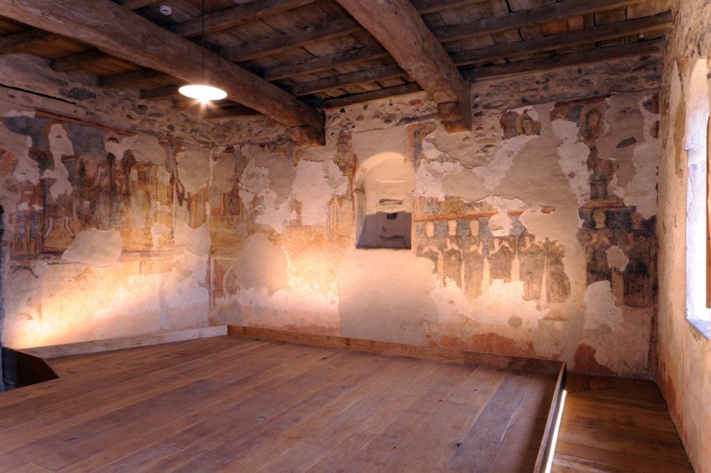 나무 대들보, 석고 벽에 새겨진 프레스코화, 나무 바닥, 매달린 조명 기구가 있는 소박한 객실입니다.