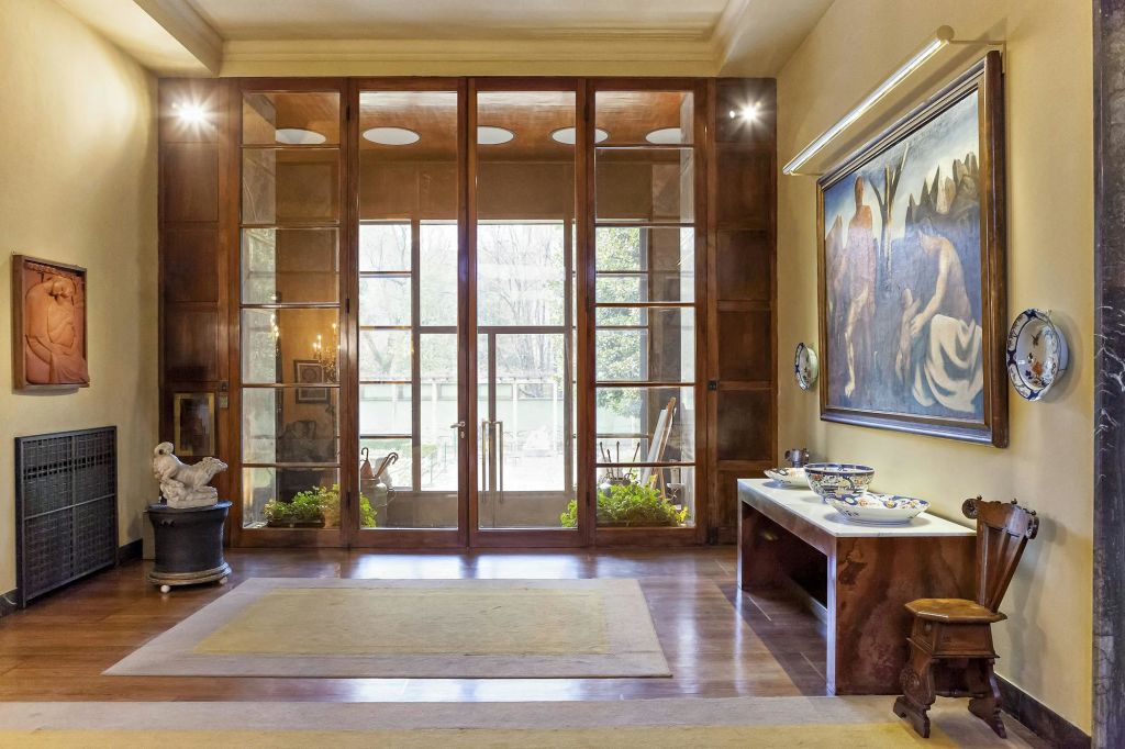 커다란 유리문이 있는 넓은 객실, 오른쪽 벽에 그림, 장식품이 놓인 테이블이 있습니다. 라이트 스트리밍이 들어옵니다.