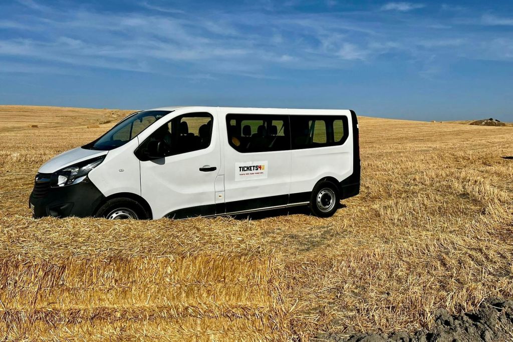 회사 로고가 새겨진 흰색 밴이 푸른 하늘 아래 건조하고 수확된 밭에 주차되어 있습니다.