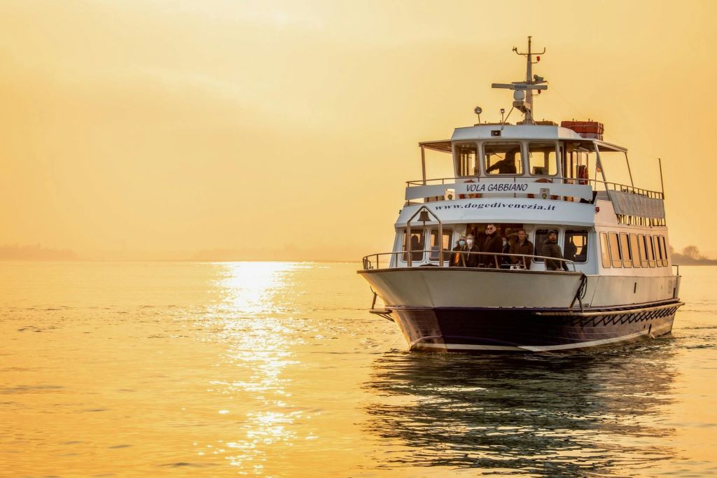 황금빛 석양의 잔잔한 물가에 있는 여객선으로, 갑판에서 개인이 경치를 감상할 수 있습니다.