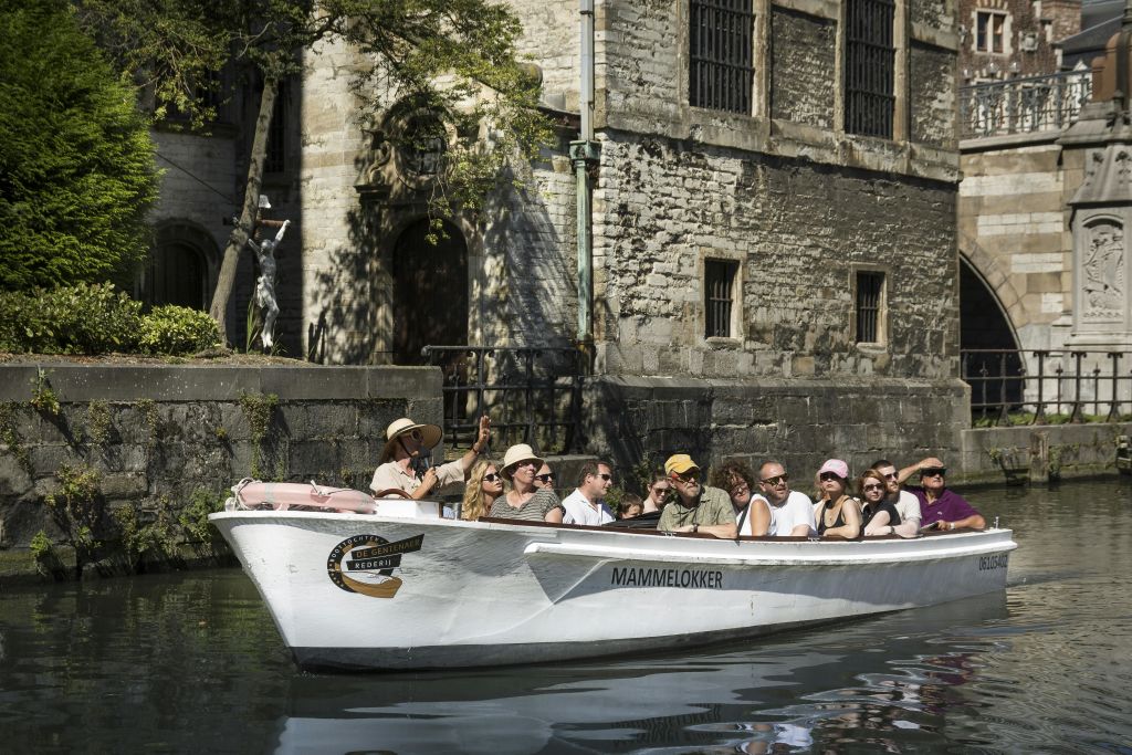 한 무리의 사람들이 하얀 보트에 앉아 화창한 날 수로를 따라 유서 깊은 석조 건물을 둘러보고 있습니다.