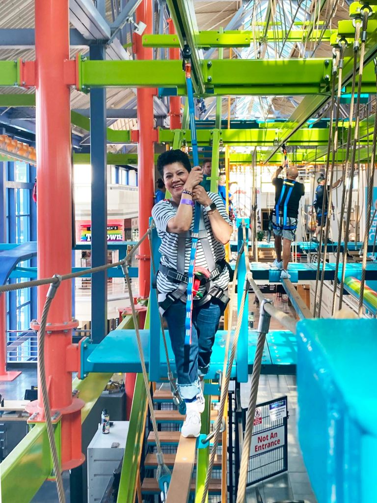 다채로운 색상의 실내 로프 코스를 거닐며 미소를 짓고 있는 하네스의 모습도 배경에서 볼 수 있습니다.