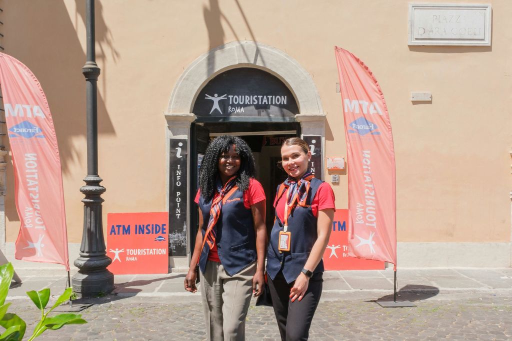 제복을 입은 두 명의 여성이 간판과 깃발이 보이는 관광 안내 센터 밖에 서 있습니다.