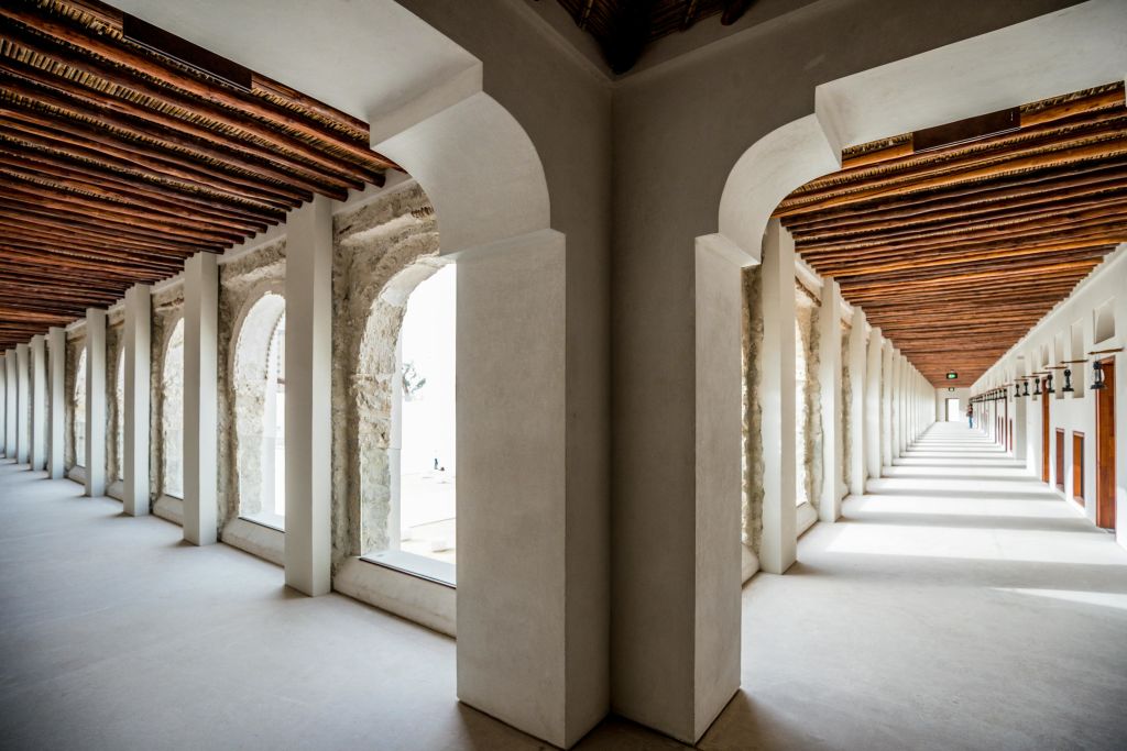 양쪽에 아치형 창문이 있는 복도로, 돌과 나무 요소가 특징이며 밝고 먼 끝점으로 뻗어 있습니다.