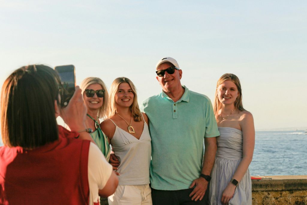 화창한 날 세 사람이 물의 몸 앞에 서 있습니다. 중앙에 있는 남자는 녹색 셔츠와 흰색 모자를 쓰고 있습니다.