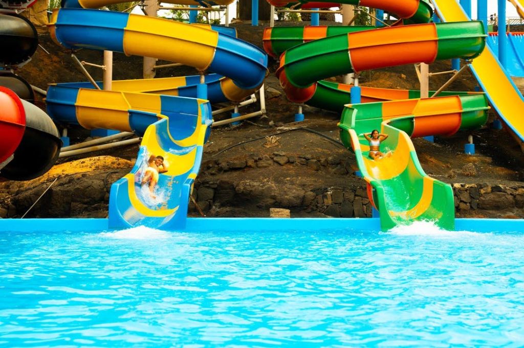 형형색색의 물 미끄럼틀을 타고 수영장으로 내려가는 두 사람. 바위 지형과 다른 미끄럼틀을 배경으로 수영을 즐겨보세요.